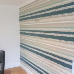 A living room corner with wooden flooring, a black leather chair on the left, and a feature wall covered in horizontal striped wallpaper in shades of teal, beige, cream, and gray highlights expert property maintenance throughout.