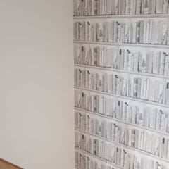 A staircase with a wooden handrail next to a wall covered in wallpaper featuring a black and white bookshelf pattern, creating the illusion of shelves filled with books—perfect inspiration for any painter and decorator.