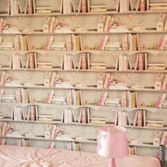 A bedroom with a bed covered in a pink sheet, a pink lamp on a bedside table, and wallpaper designed to look like bookshelves filled with pastel-colored books and small ornaments—ideal inspiration for any painter and decorator.