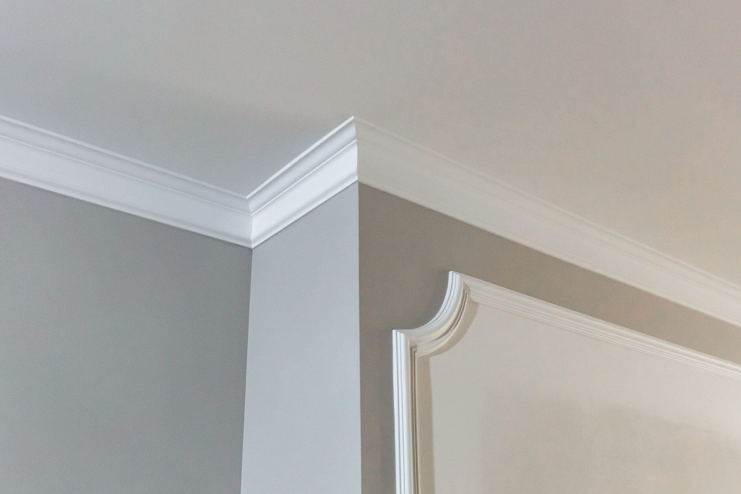 A close-up view of an interior room corner with light gray walls, white crown molding along the ceiling, and decorative trim detail—showcasing the results of expert property maintenance.